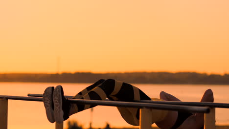 Candid-shot-of-real-healthy-and-fit-woman-performing-hanging-leg-raises-on-outdoor-fitness-station-in-sunset-at-beach-promenade.-Showing-strong-abdominal-six-pack.